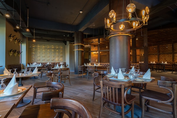 A restaurant with wooden tables and chairs, hanging light fixtures, and a brick wall. - Punta Cana Princess Adults Only - All Inclusive (Punta Cana)