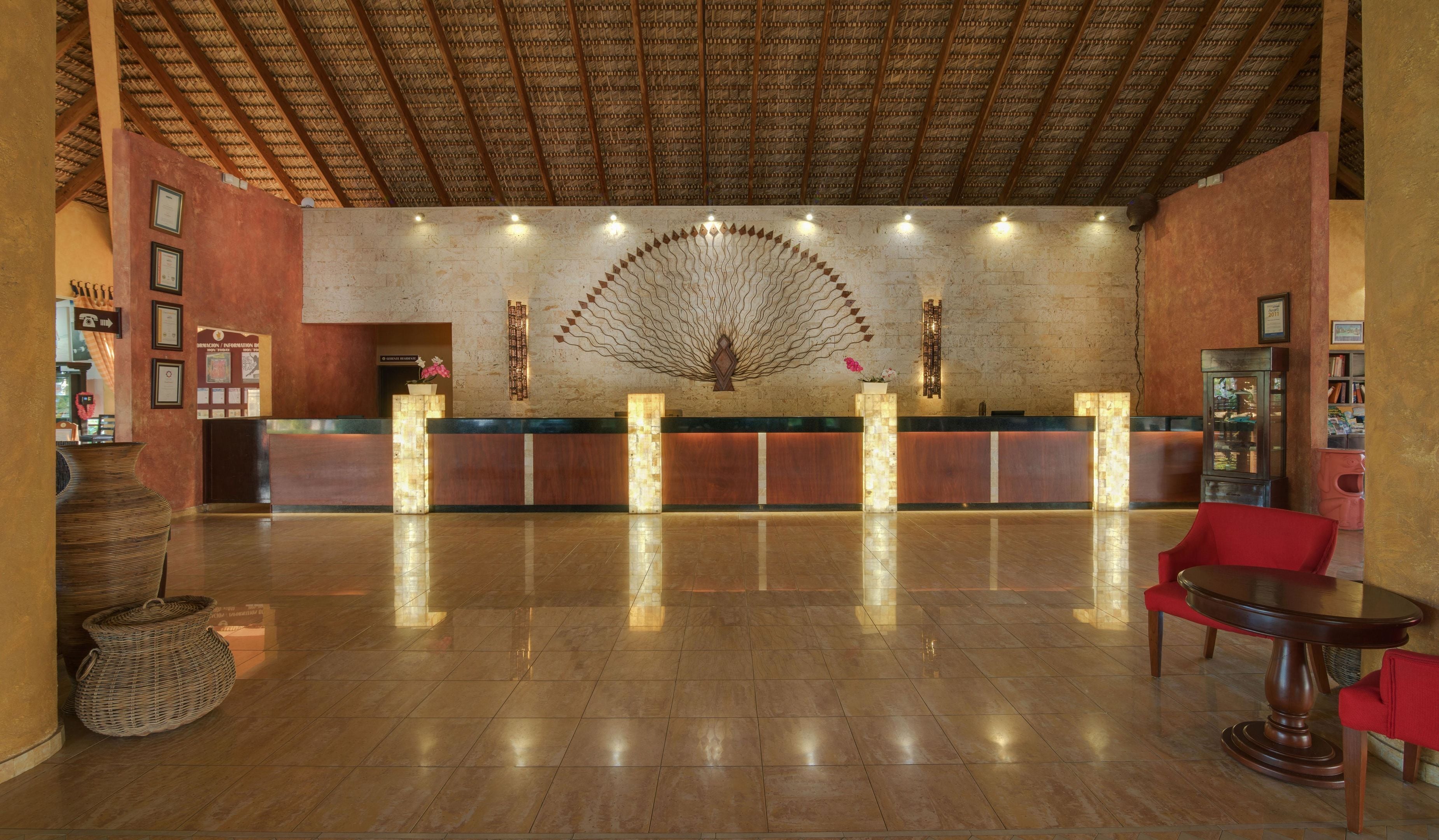 A hotel reception area with a central desk, a large decorative fan, and a polished tile floor.