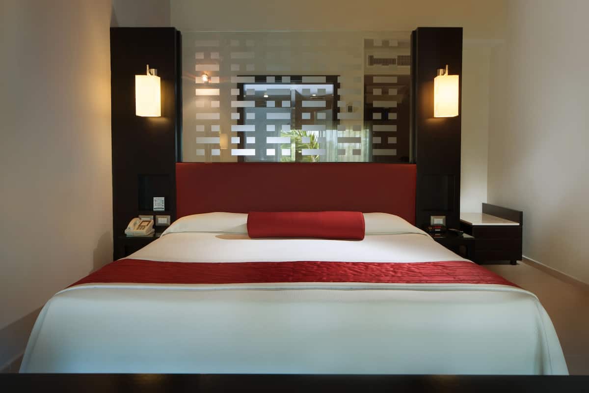 Ein modernes Hotelzimmer mit einem großen Bett, roter Bettwäsche und zwei an der Wand befestigten Nachttischen.