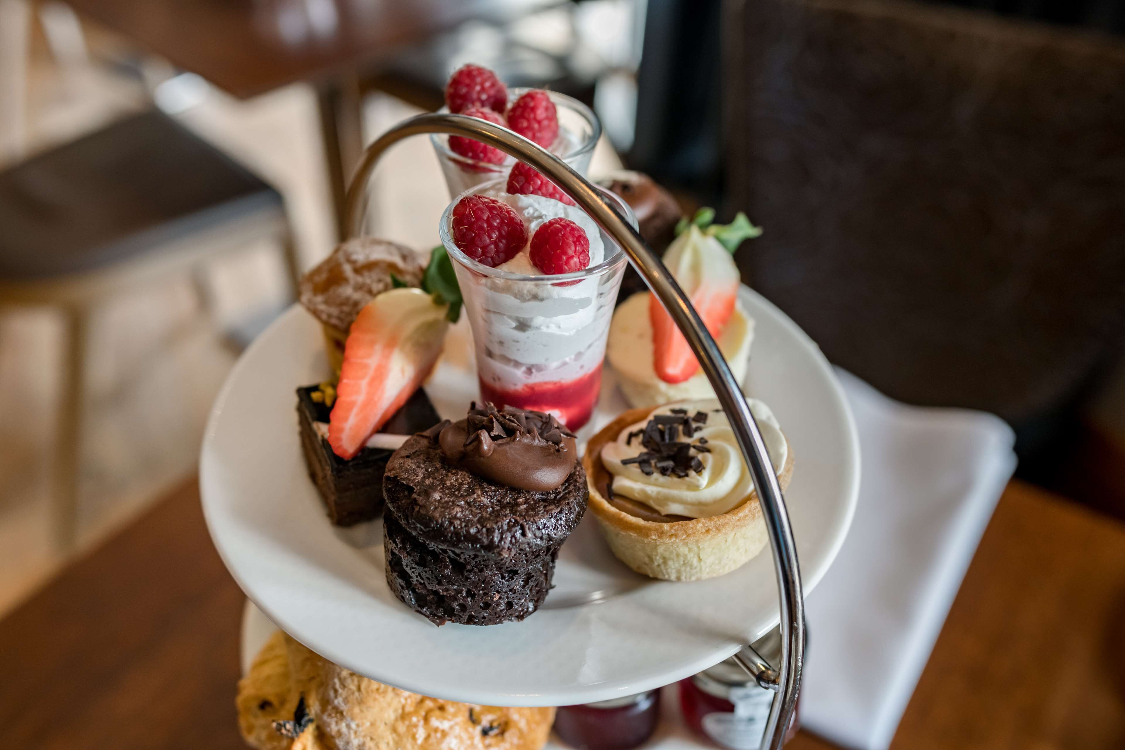A dessert tray with various pastries and a glass of dessert topped with raspberries.