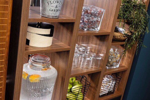 A wooden shelf with various items including a jar with lemons, a basket of apples, and several glass containers.