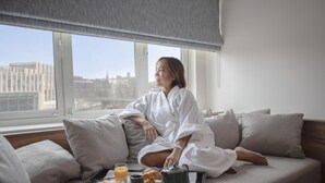 A person sitting on a sofa with a tray of breakfast items in front of a window with a city view.