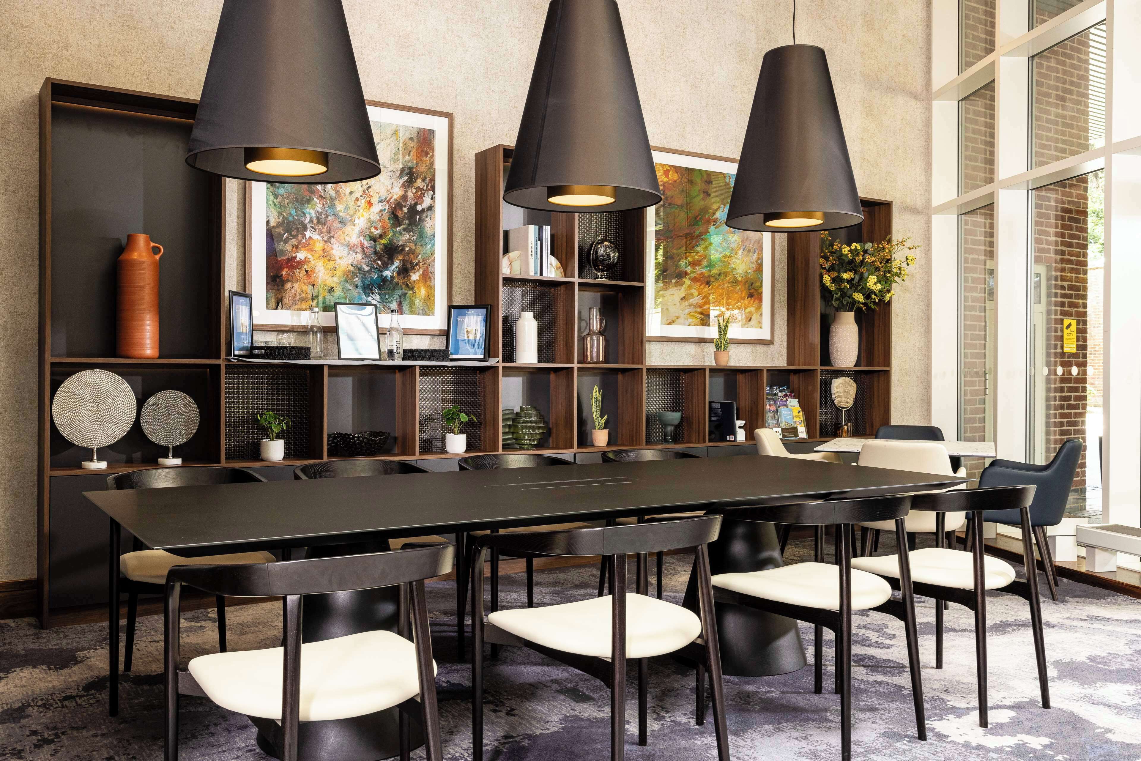 A modern dining area with a long table, black chairs, and pendant lighting.
