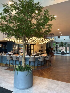 A modern bar area with a large tree in a planter, hanging light fixtures, and a bar counter with stools.