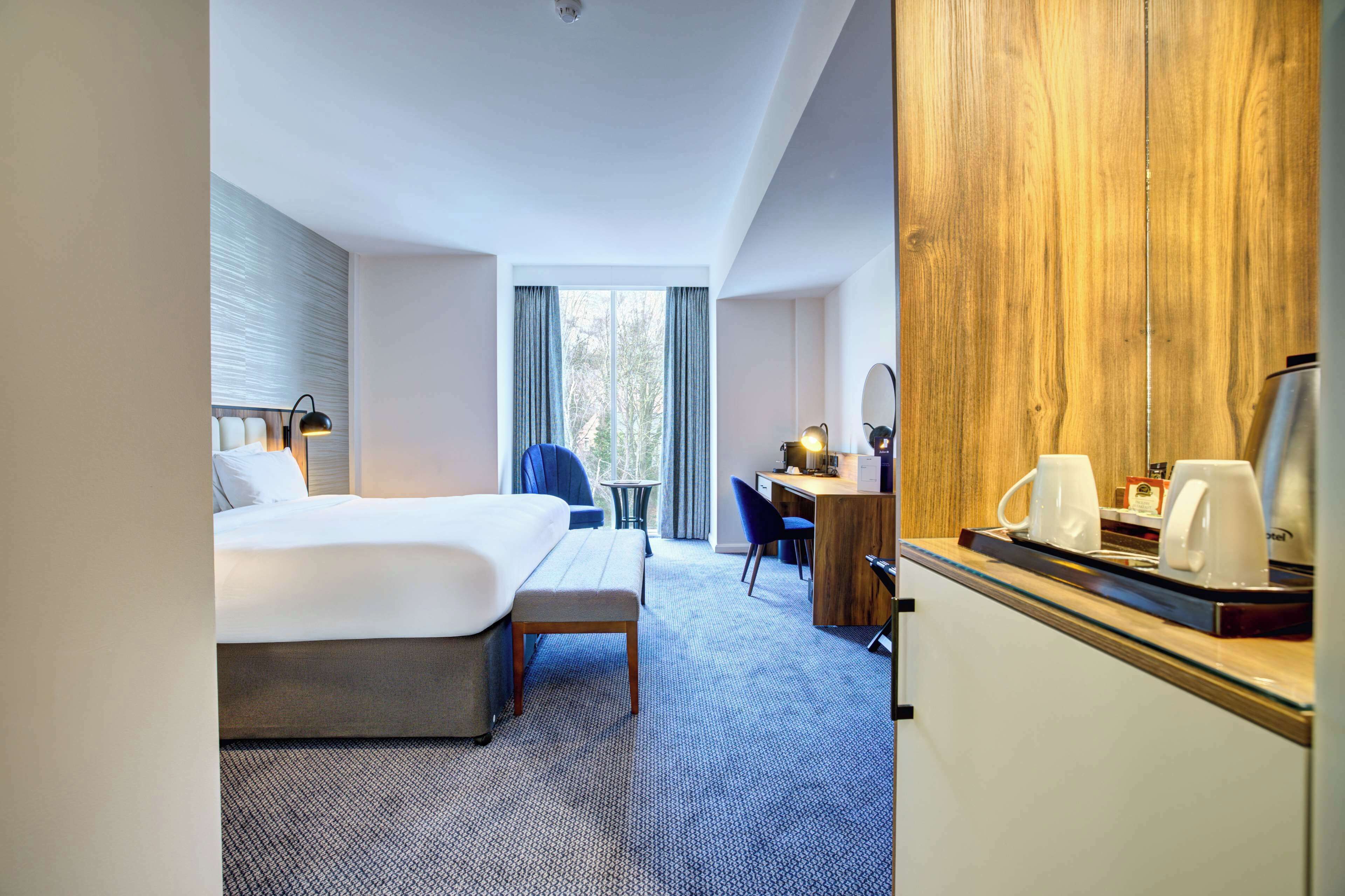 A hotel room with a bed, a desk, a chair, a small table, and a wardrobe.