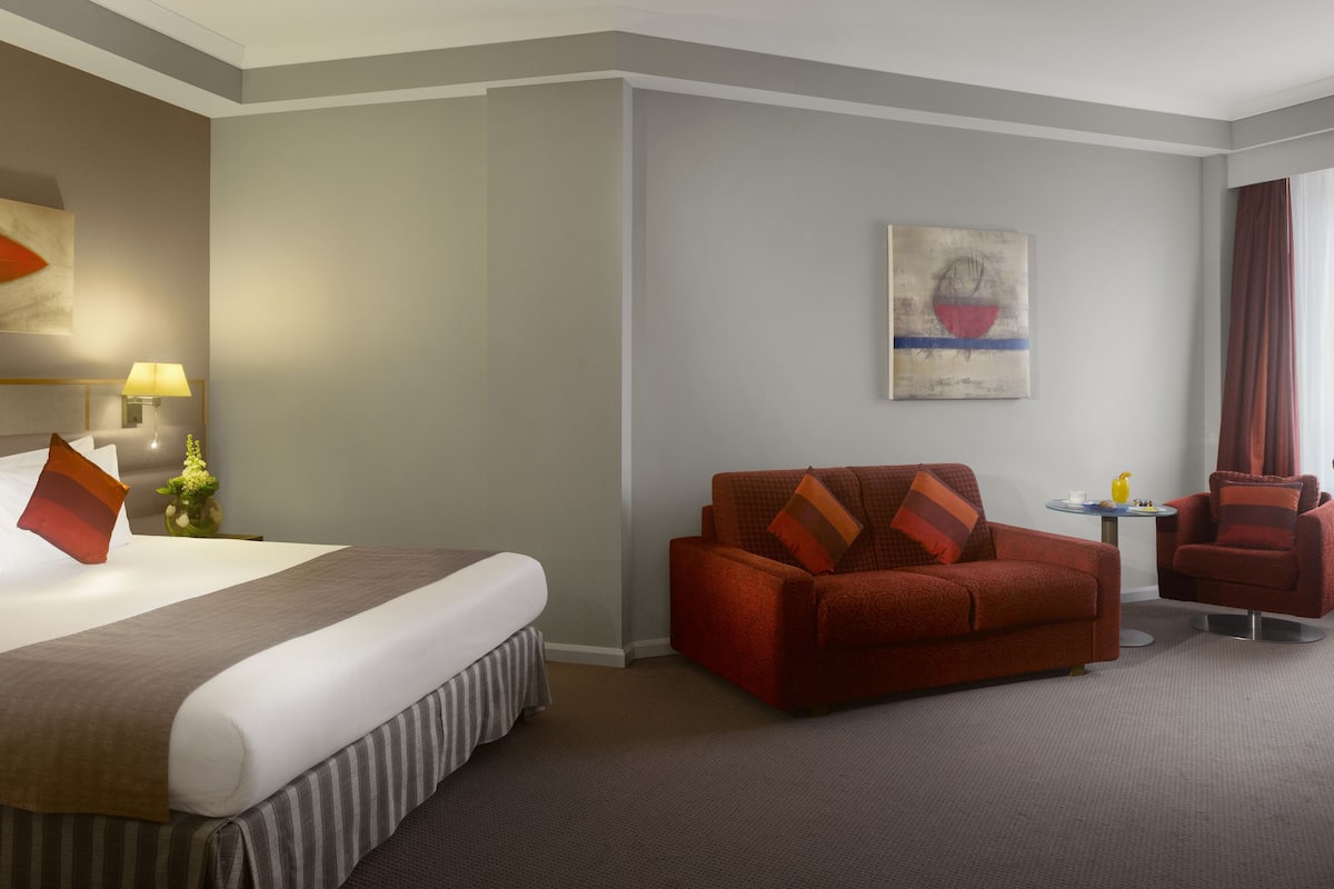 Une chambre d’hôtel avec un lit, un canapé rouge, une petite table ronde et une chaise.