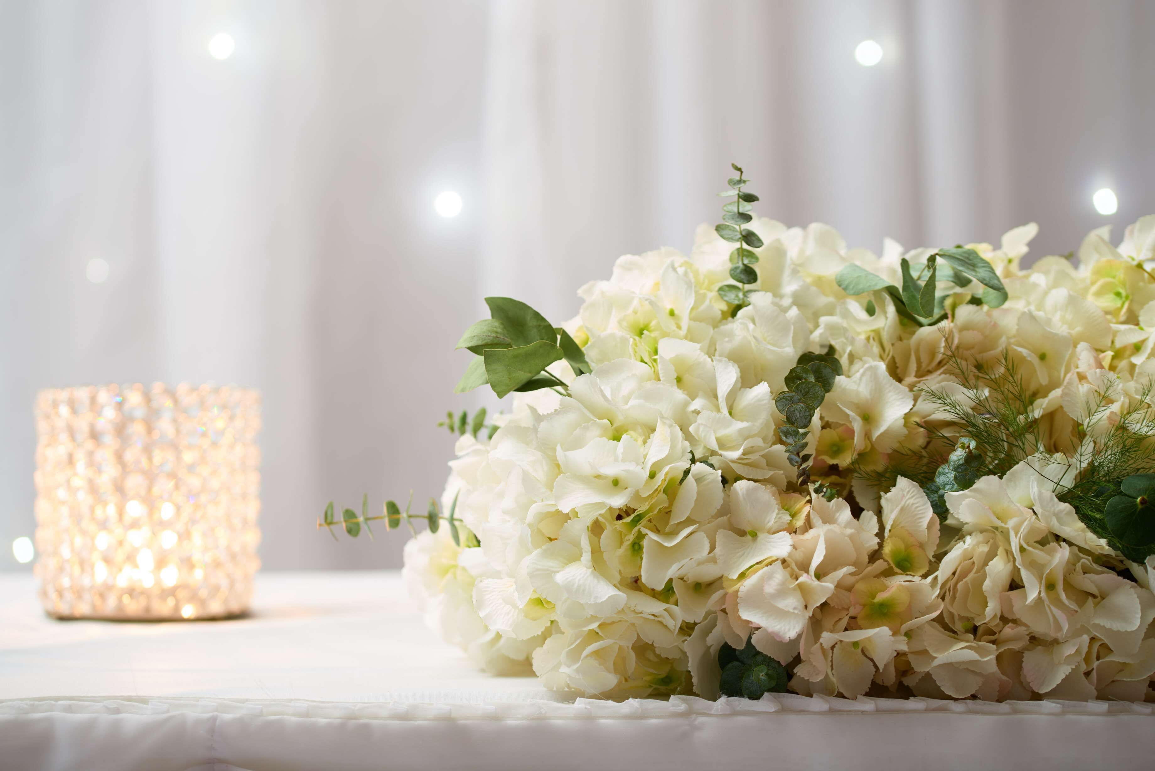 Een boeket witte bloemen en een brandende kaars op een tafel.