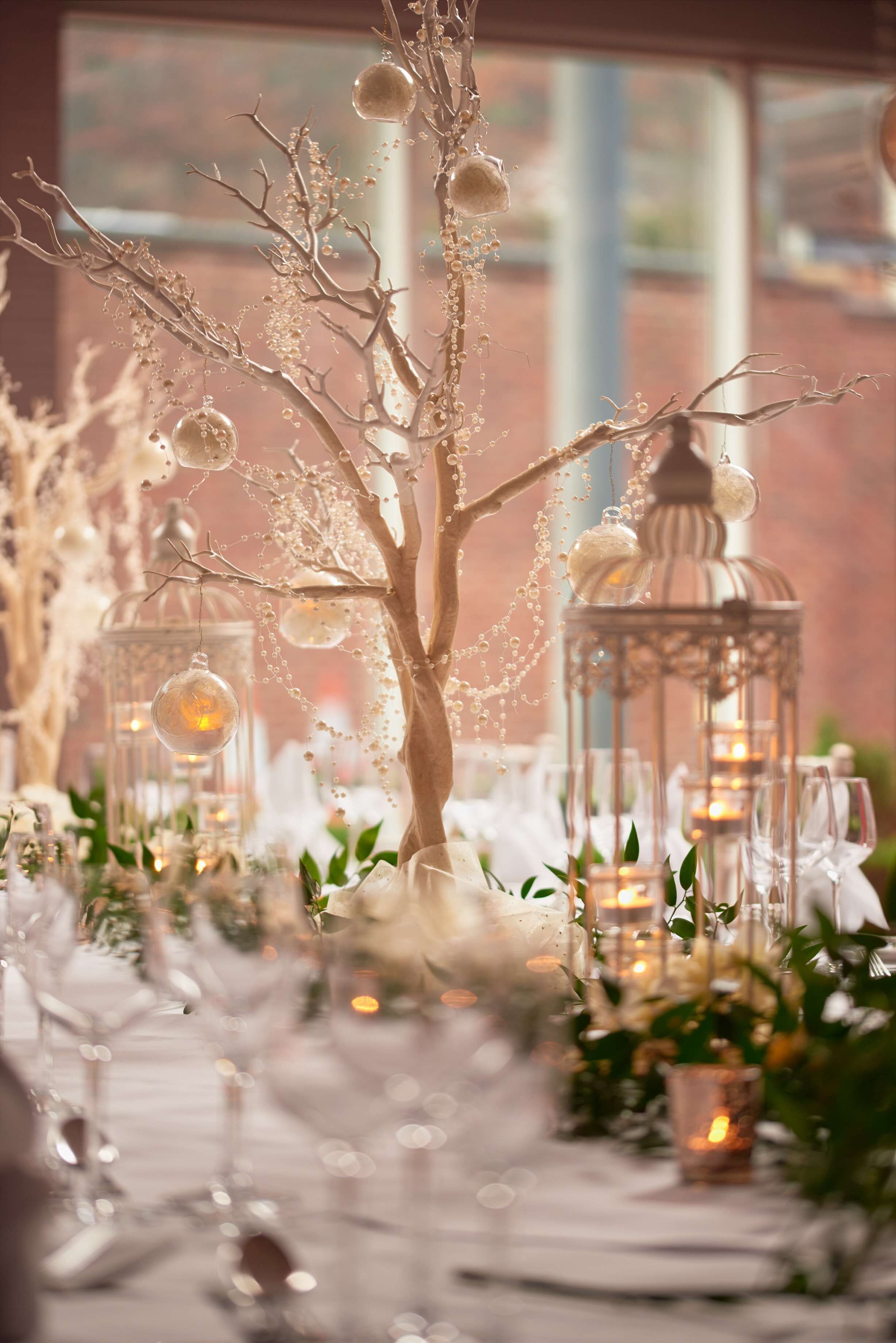 Una mesa dispuesta con cristalería, velas y un centro de mesa decorativo con un árbol.