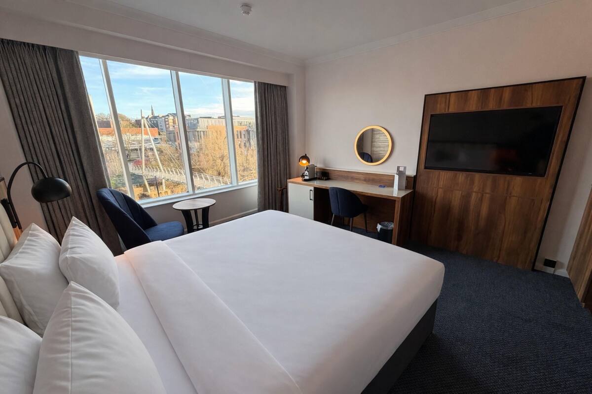 Une chambre d’hôtel avec un grand lit, un bureau, une chaise, une télévision et une vue sur les immeubles par la fenêtre.