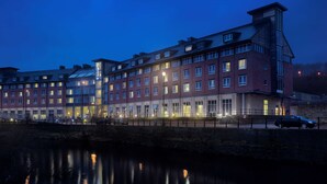 A multi-story hotel with a brick facade and large windows, reflecting in a body of water.