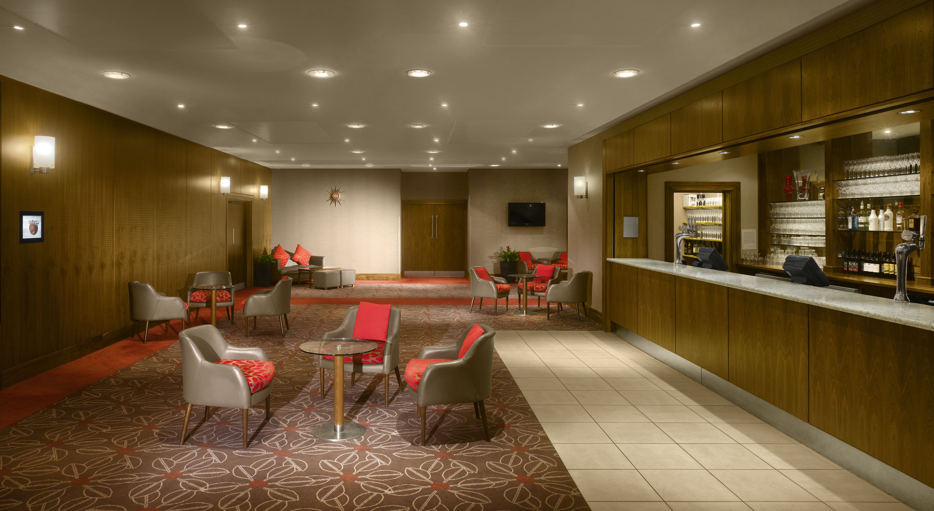 A hotel lobby with a bar area, seating arrangements, and a television screen.