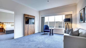 A hotel room with a bed, a sofa, a chair, a TV, and a large window with a city view.
