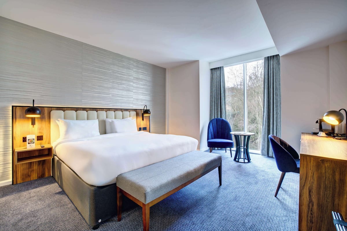 Une chambre d’hôtel avec un grand lit, un banc, un bureau et une chaise.