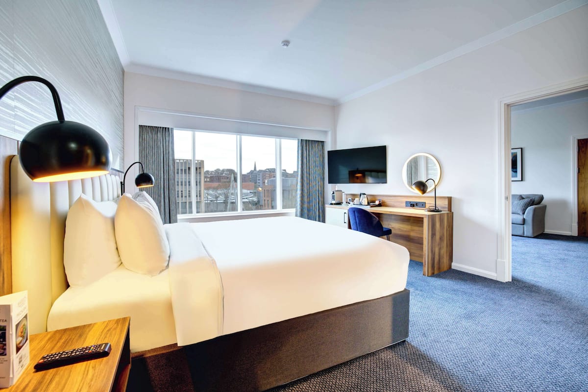 Ein Hotelzimmer mit einem großen Bett, einem Schreibtisch, einem Fernseher und Blick auf die Stadt durch das Fenster.