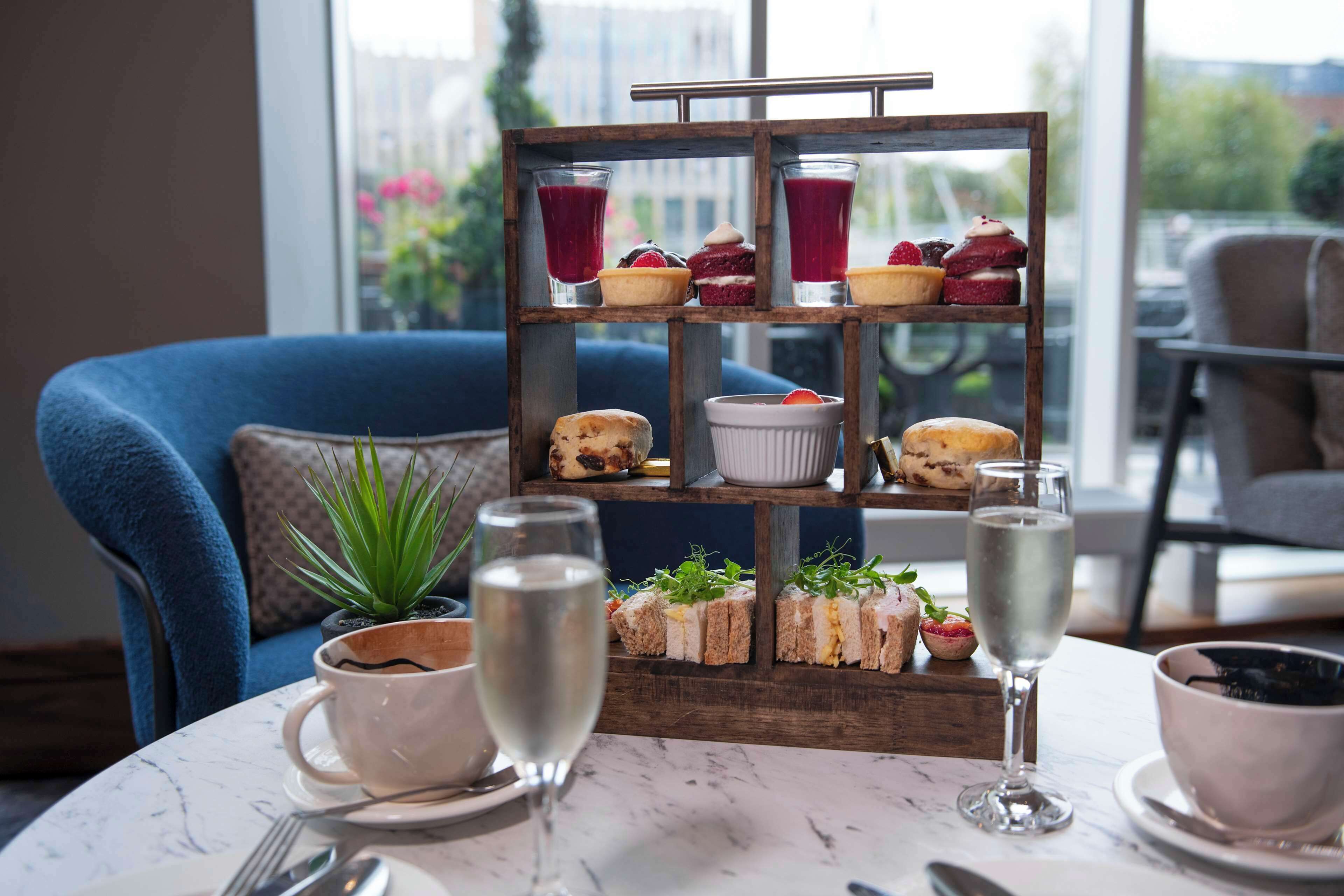 A table with a tiered dessert stand, a potted plant, and two glasses of a clear liquid, likely water or champagne, on a marble table.