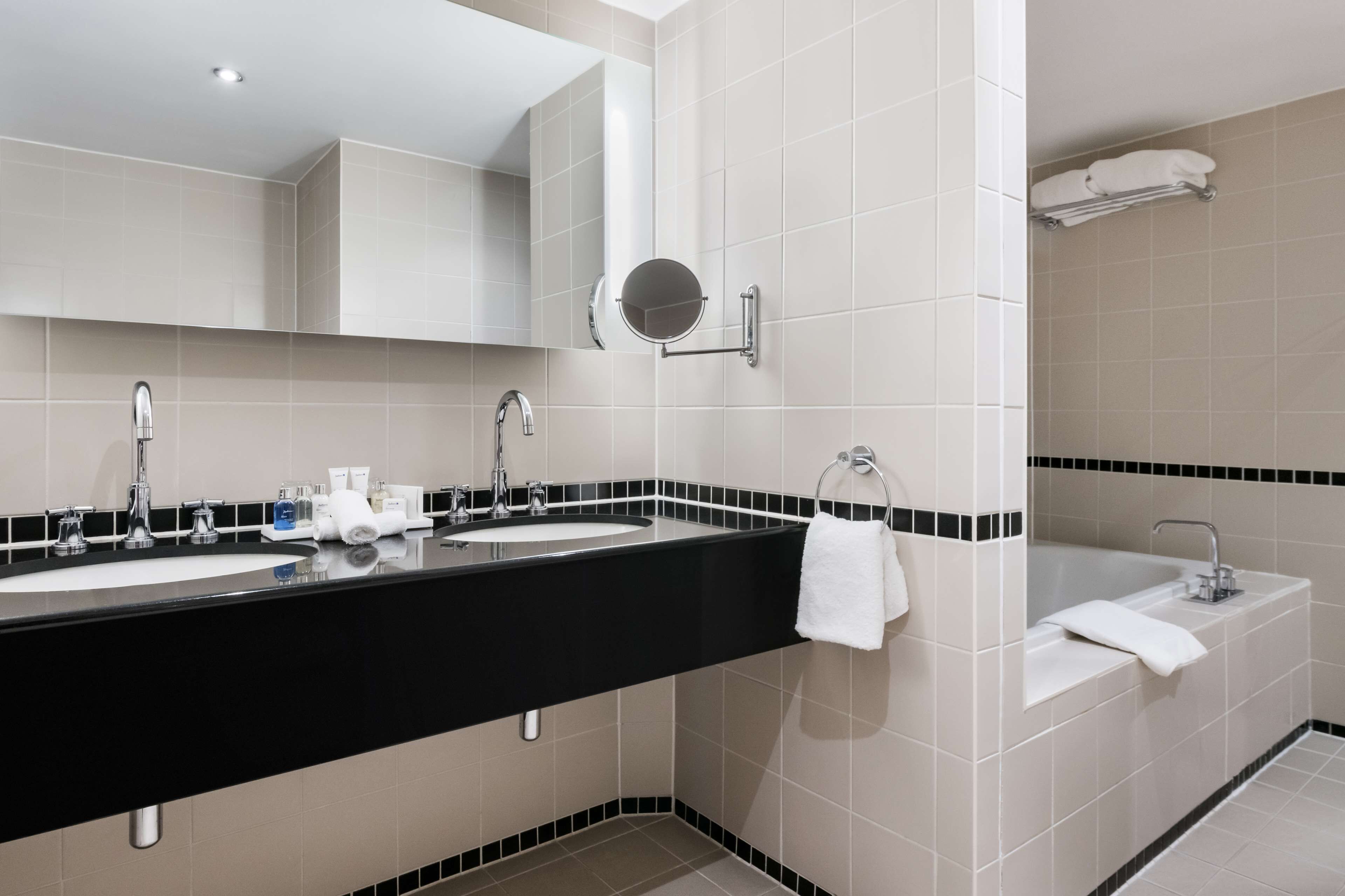 A modern bathroom with two sinks, a large mirror, and a bathtub.