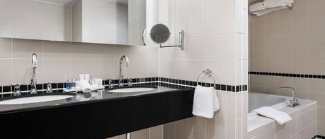 A modern bathroom with two sinks, a large mirror, and a bathtub.