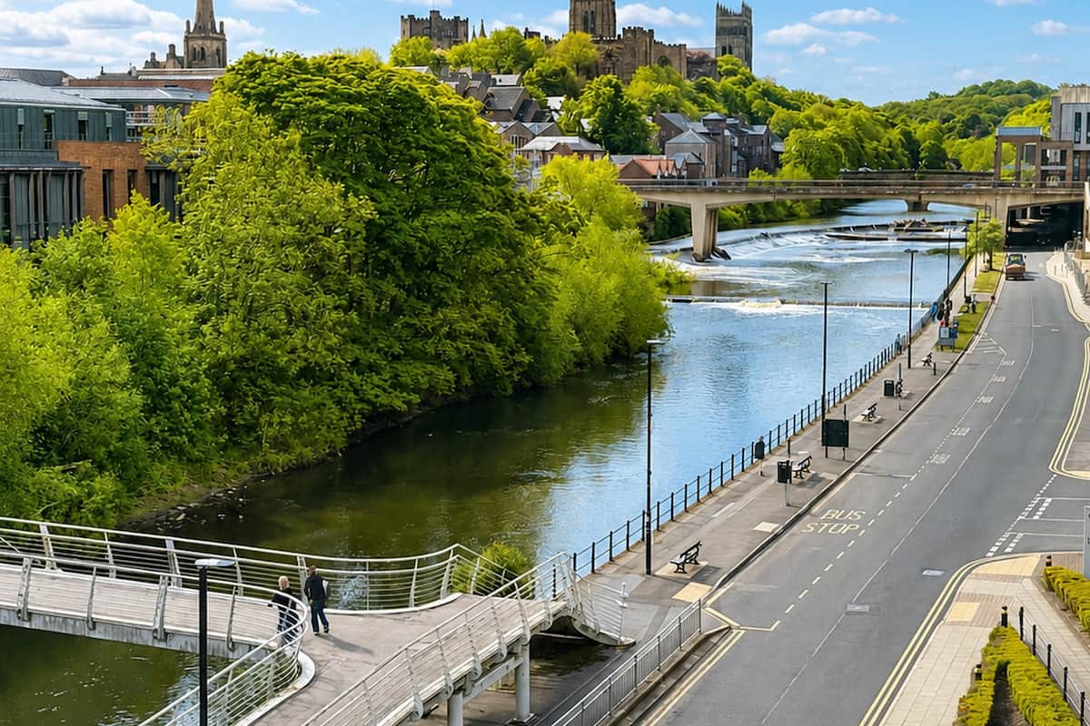 Eine Flussuferstraße mit einer Fußgängerbrücke, einem Fluss und Gebäuden im Hintergrund.