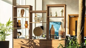 A modern interior with a blue armchair, wooden shelving with decorative items, and a large window.