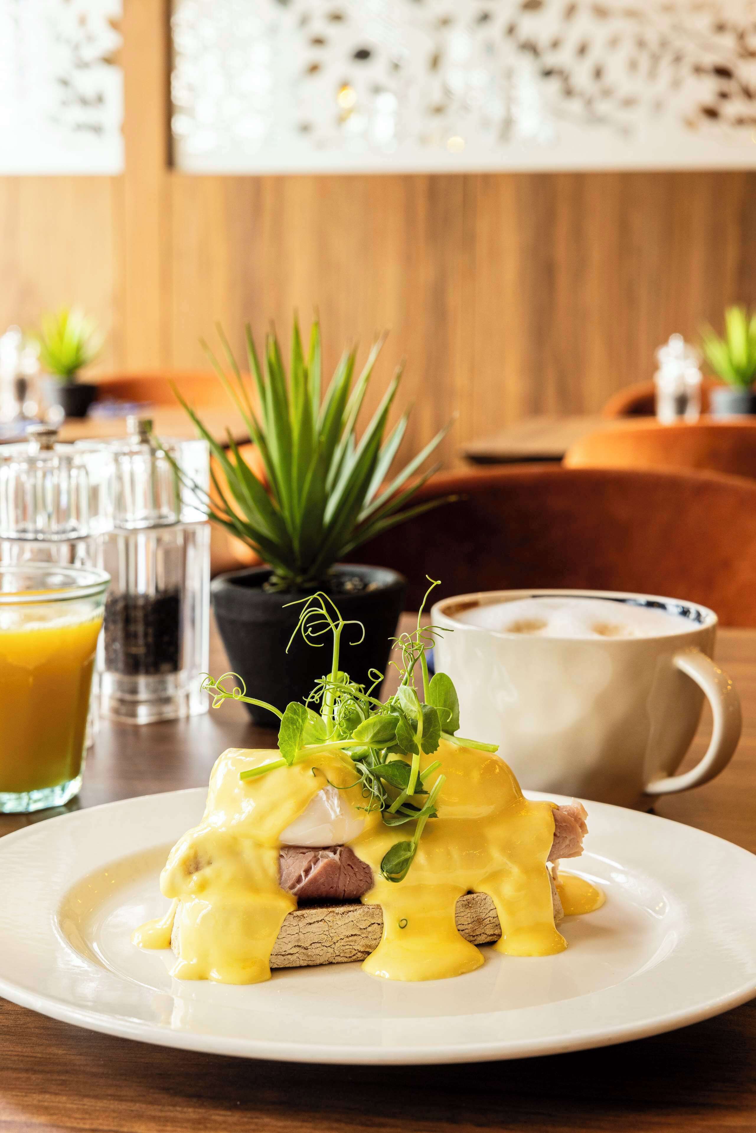 A breakfast setting with a plate of eggs benedict, a coffee cup, and a glass of orange juice.