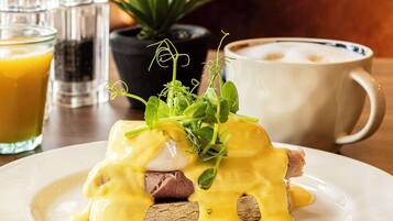 A breakfast setting with a plate of eggs benedict, a coffee cup, and a glass of orange juice.