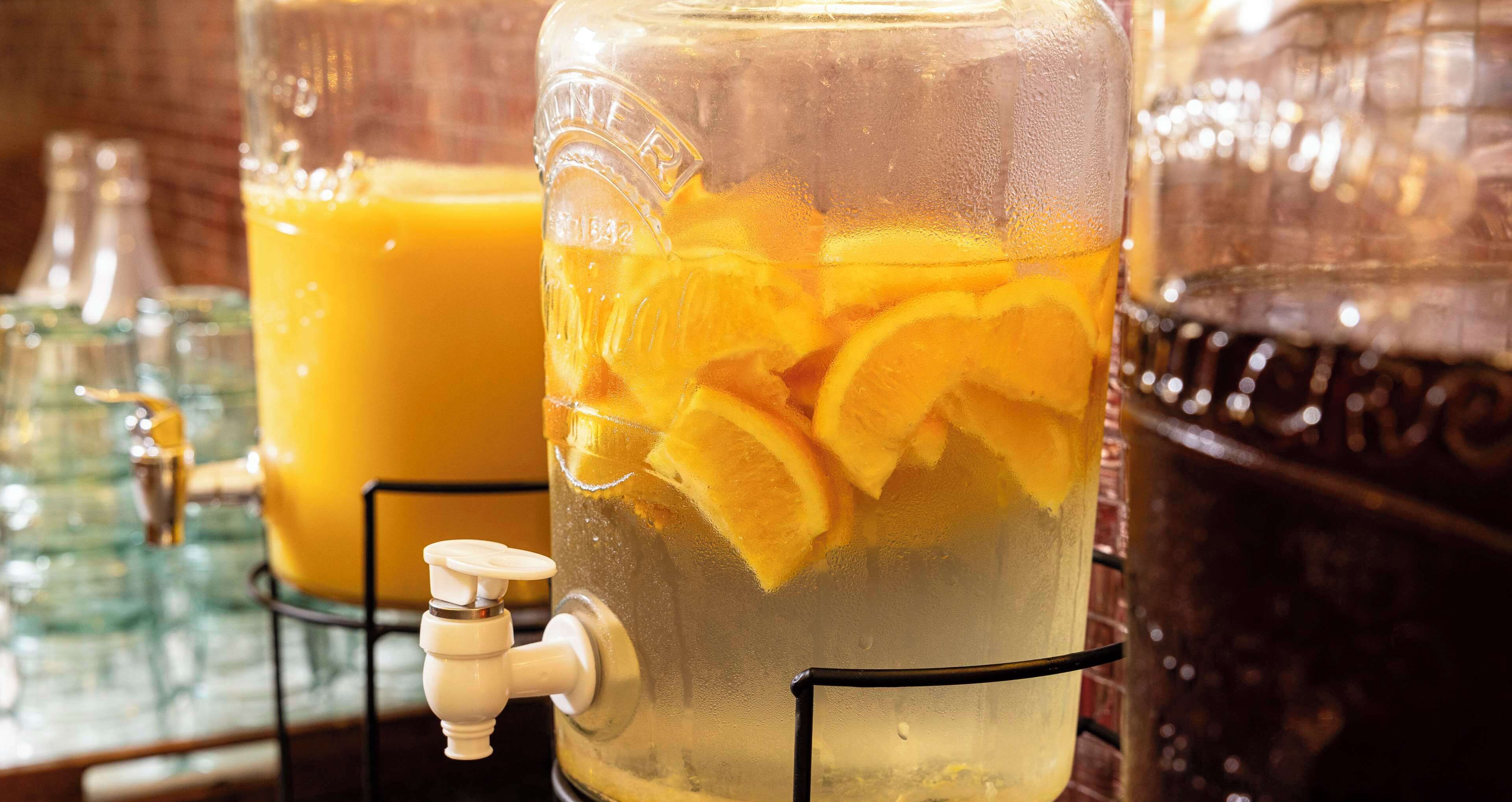 A large glass container with a tap, filled with a beverage and orange slices, likely for serving at an event or gathering.