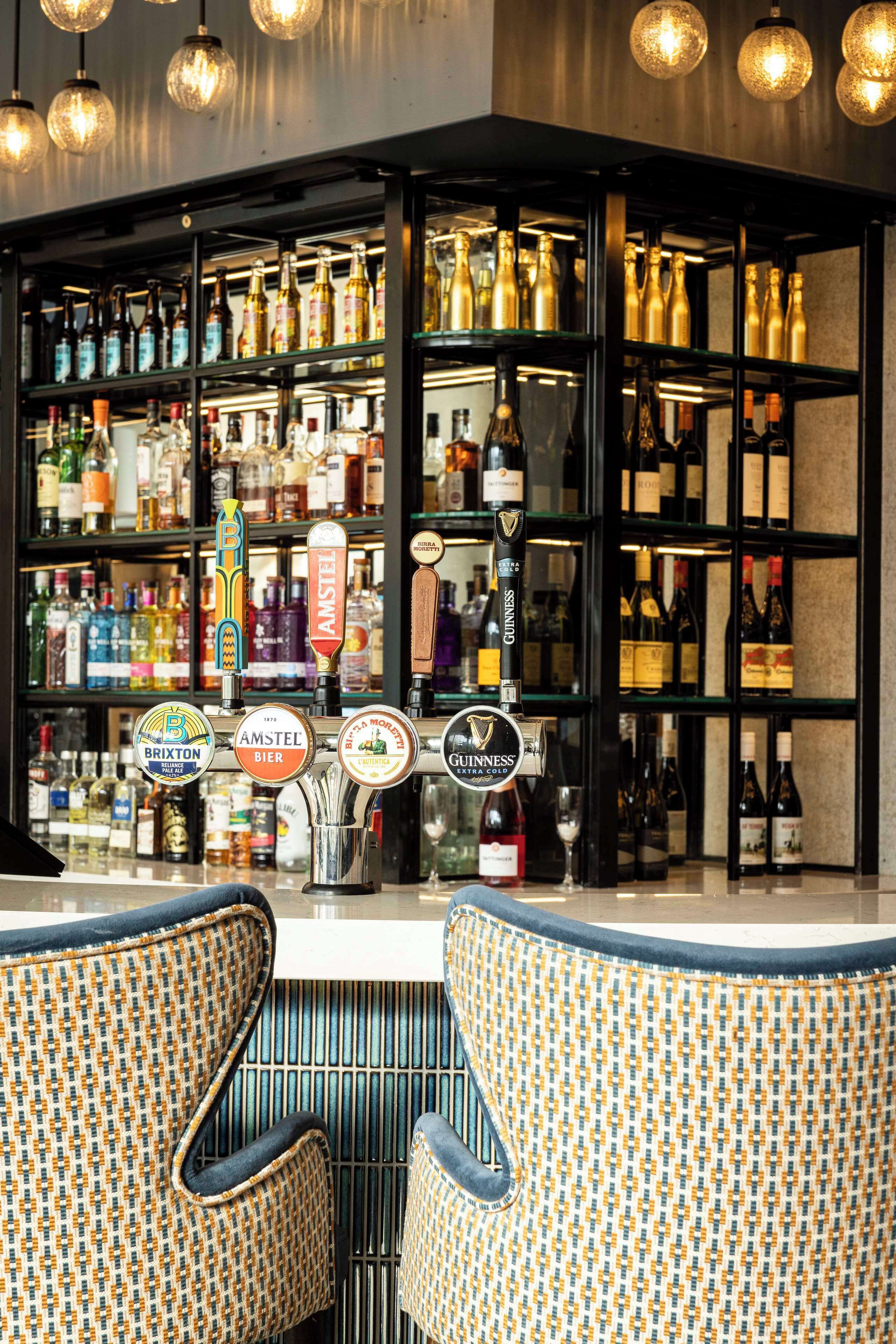Angolo bar con diverse bottiglie di liquore, varie spine di birra e due poltrone a fantasia.