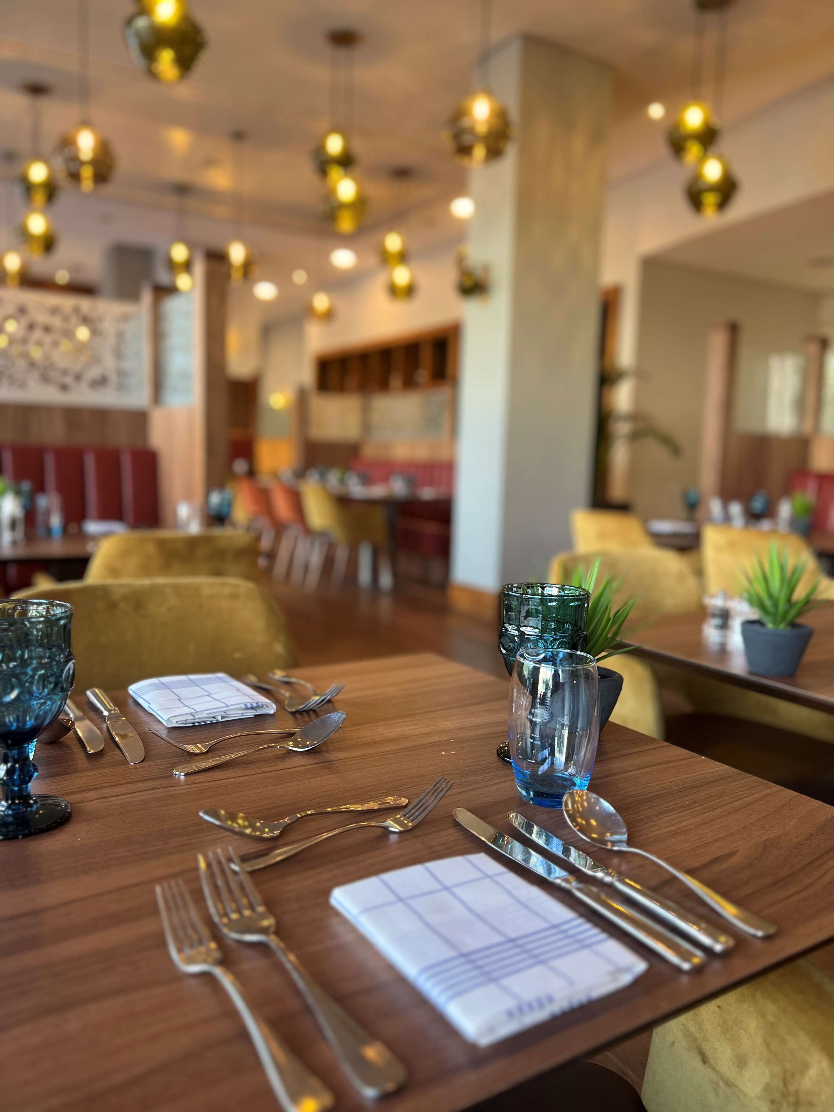 A dining table set with cutlery and a menu, surrounded by chairs and a potted plant.