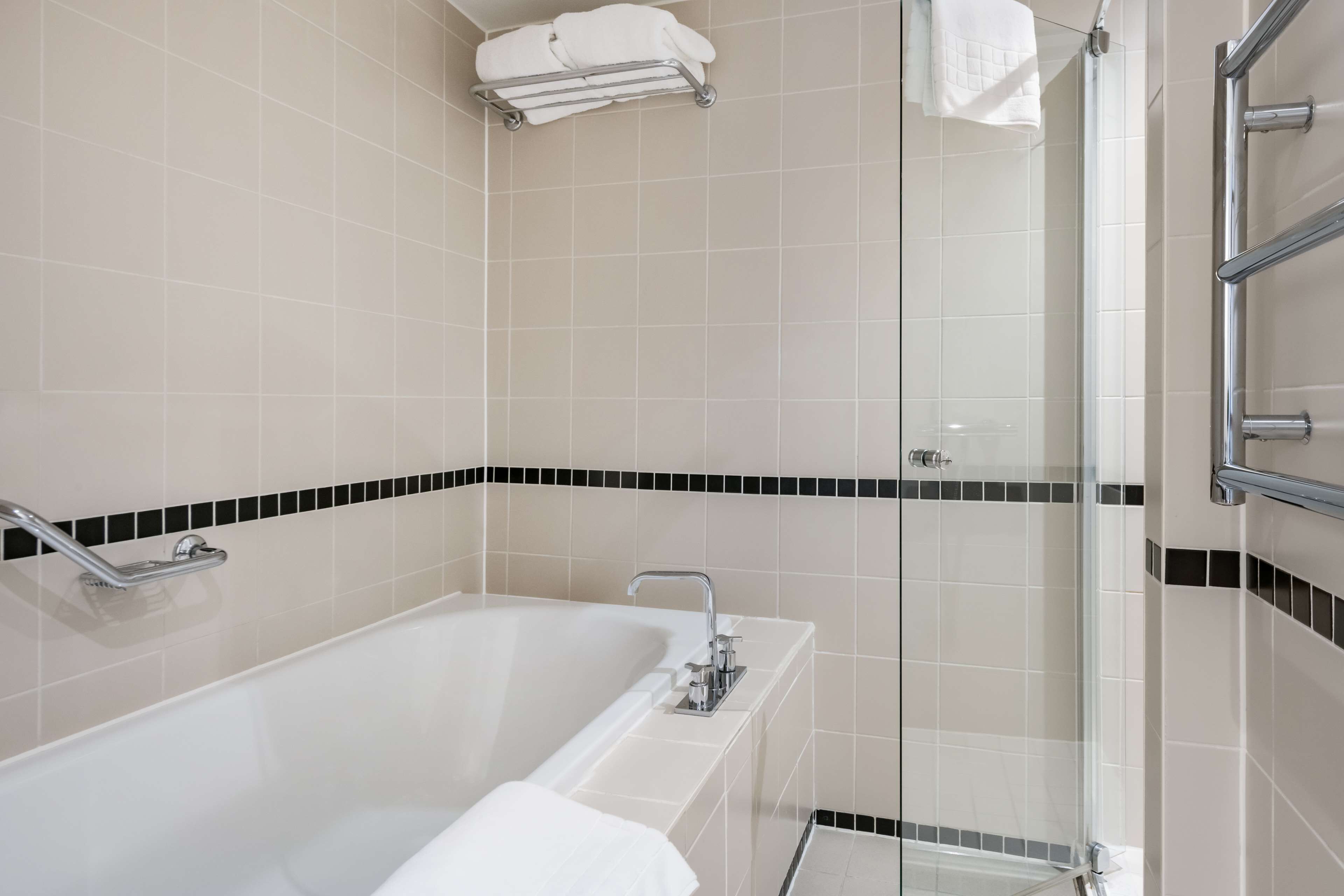 A modern bathroom with a bathtub, a glass shower enclosure, and a towel rack.