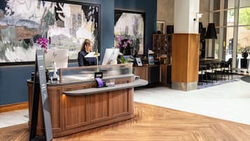 A reception desk with a computer, a vase with purple flowers, and a large abstract painting on the wall.