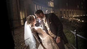A couple embracing on a nighttime outdoor area with a building in the background.