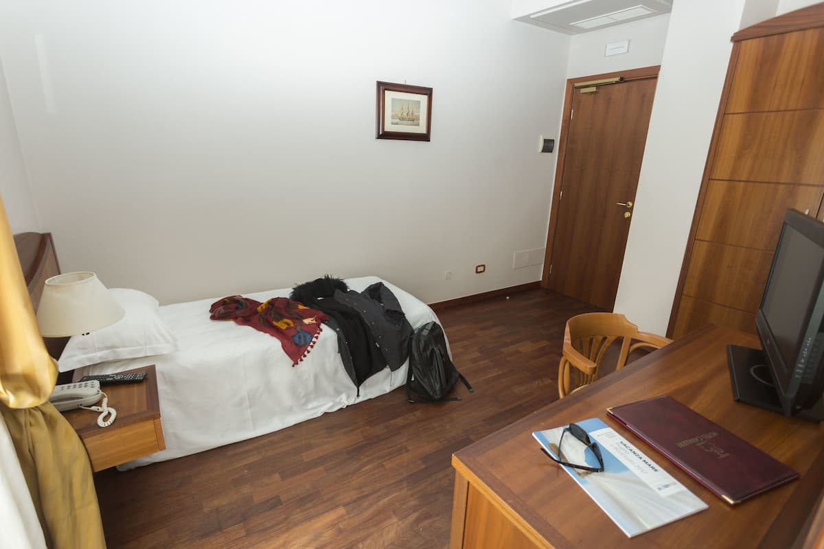 A hotel room with a bed, a desk with a computer, a chair, a television, and a wardrobe.