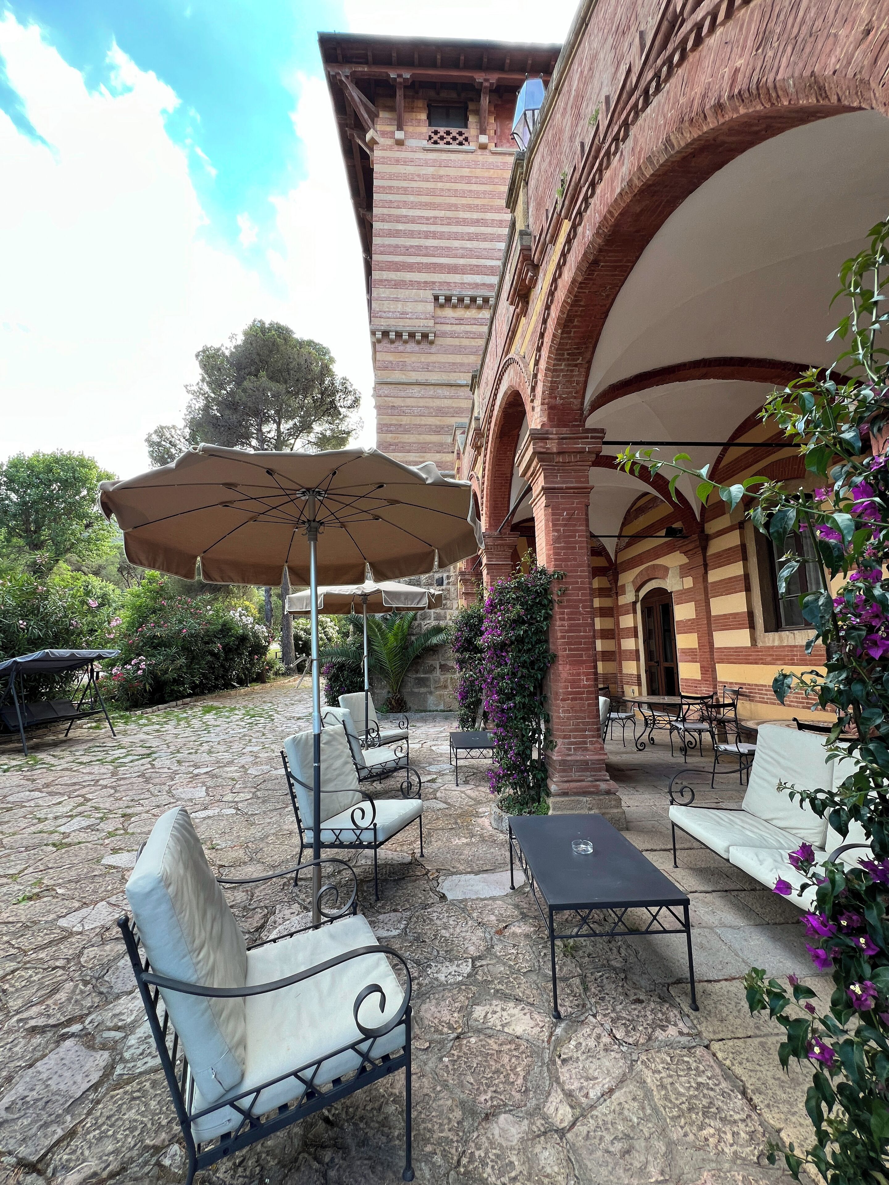Un patio al aire libre con piso de piedra, sillas metálicas, una mesa y una sombrilla.