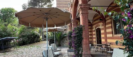 Un patio al aire libre con piso de piedra, sillas metálicas, una mesa y una sombrilla.