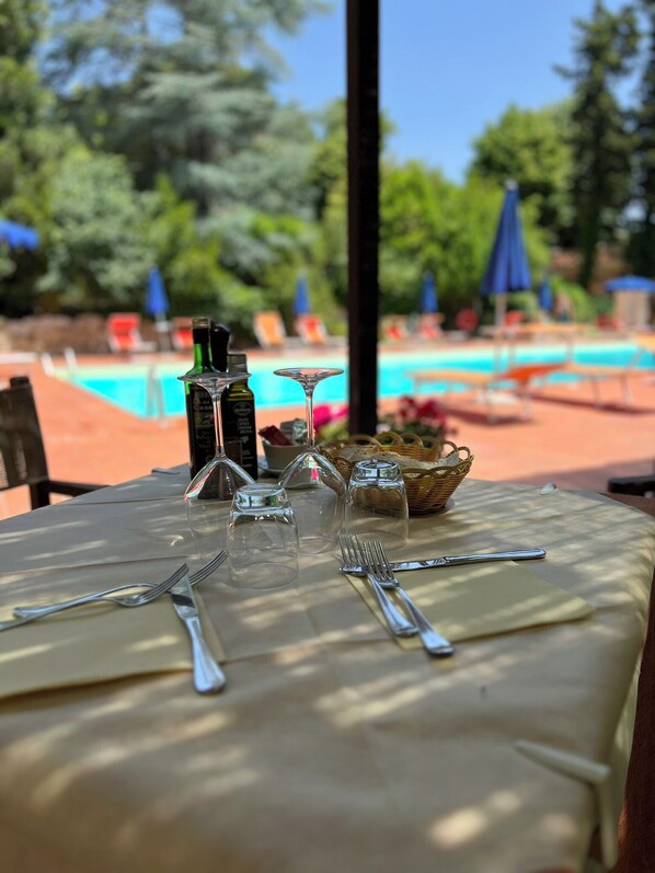 A dining table set outdoors with a pool in the background. - Park Hotel Napoleone (Portoferraio)