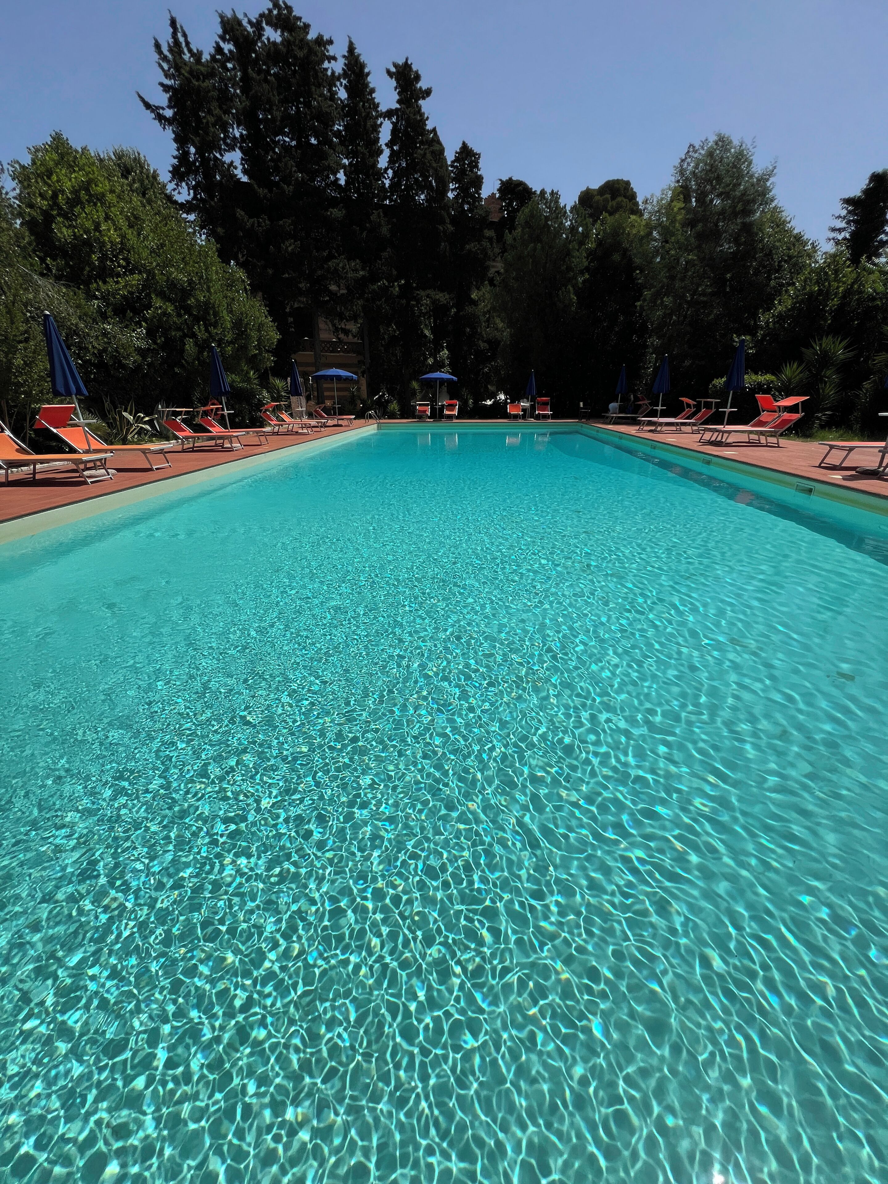 En klar swimmingpool med liggestole og parasoller hele vejen rundt.