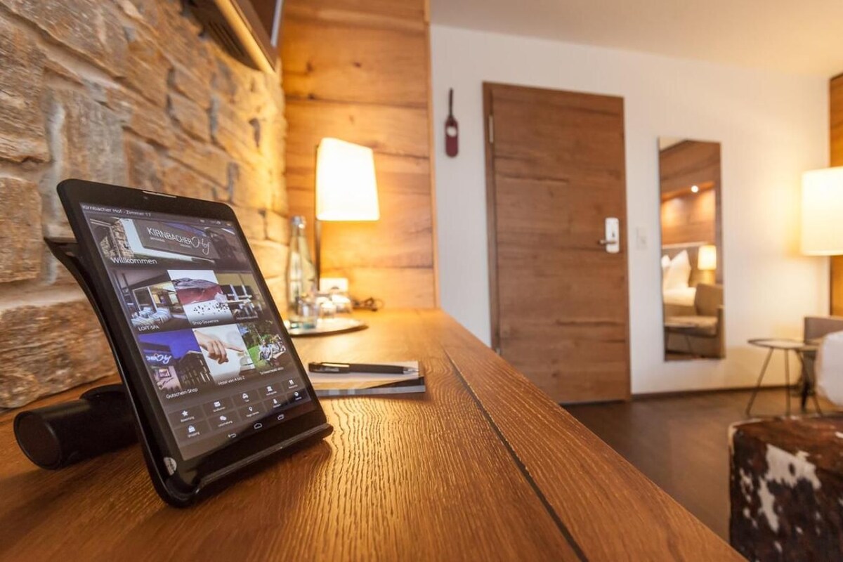 A hotel room with a wooden desk, a tablet displaying a room service menu, a bed with a cow print blanket, and a wooden headboard.