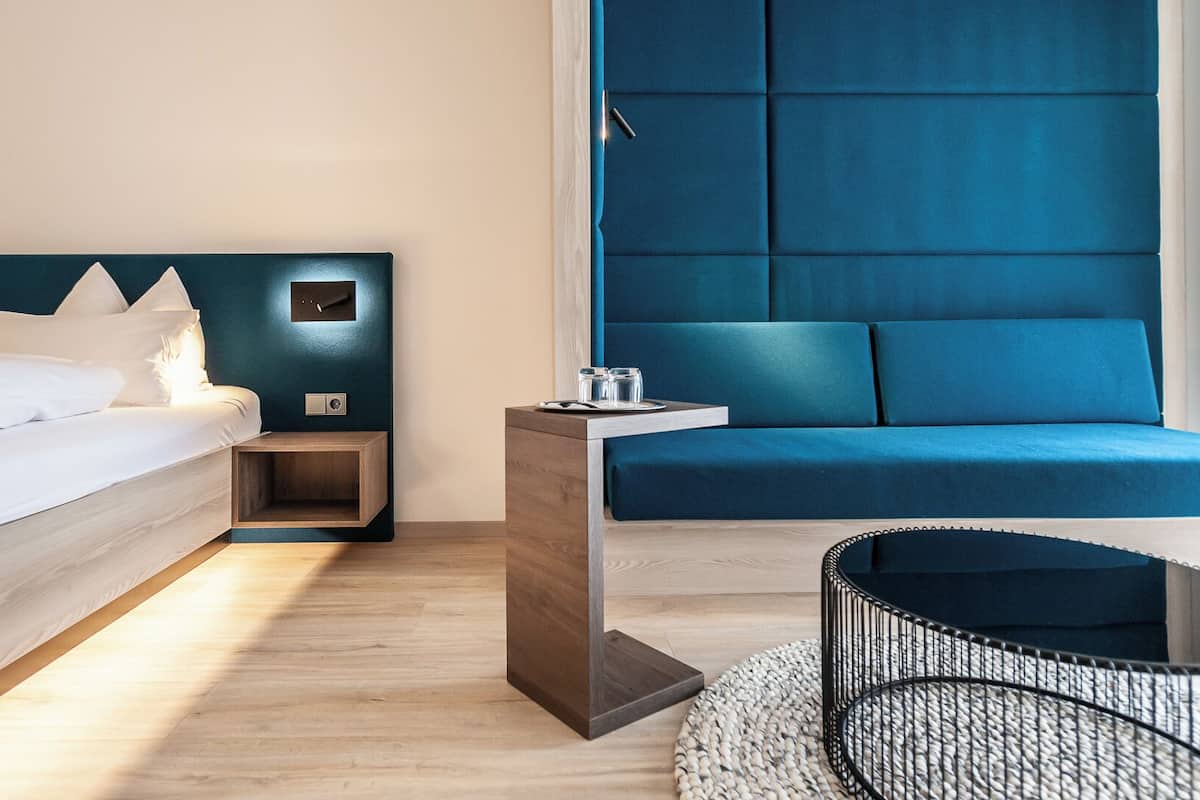 A modern hotel room with a bed, bedside table, and a blue sofa.
