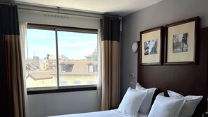 Una habitació d'hotel amb un llit gran, una finestra amb cortines i dos quadres al mur.