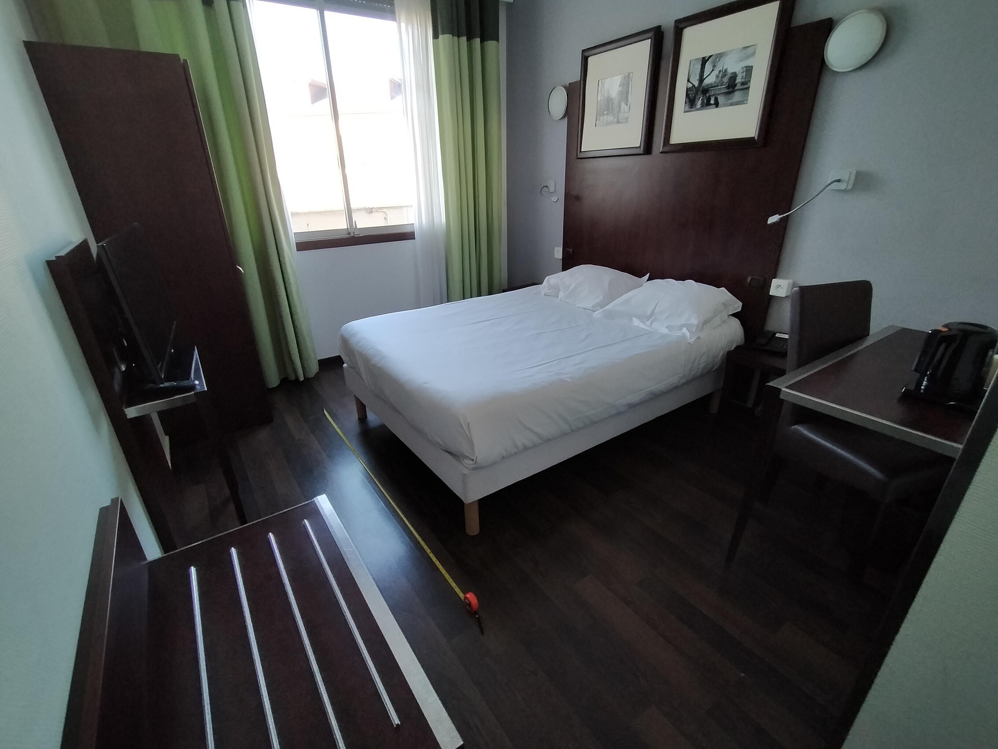 Quarto de hotel com cama, escrivaninha com cadeira, máquina de café, televisão e janela com cortinas.