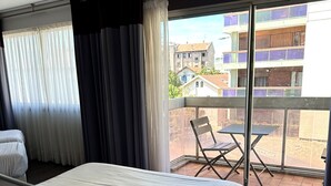 Habitació d'hotel amb un llit gran, una cadira i un balcó que dona a edificis.