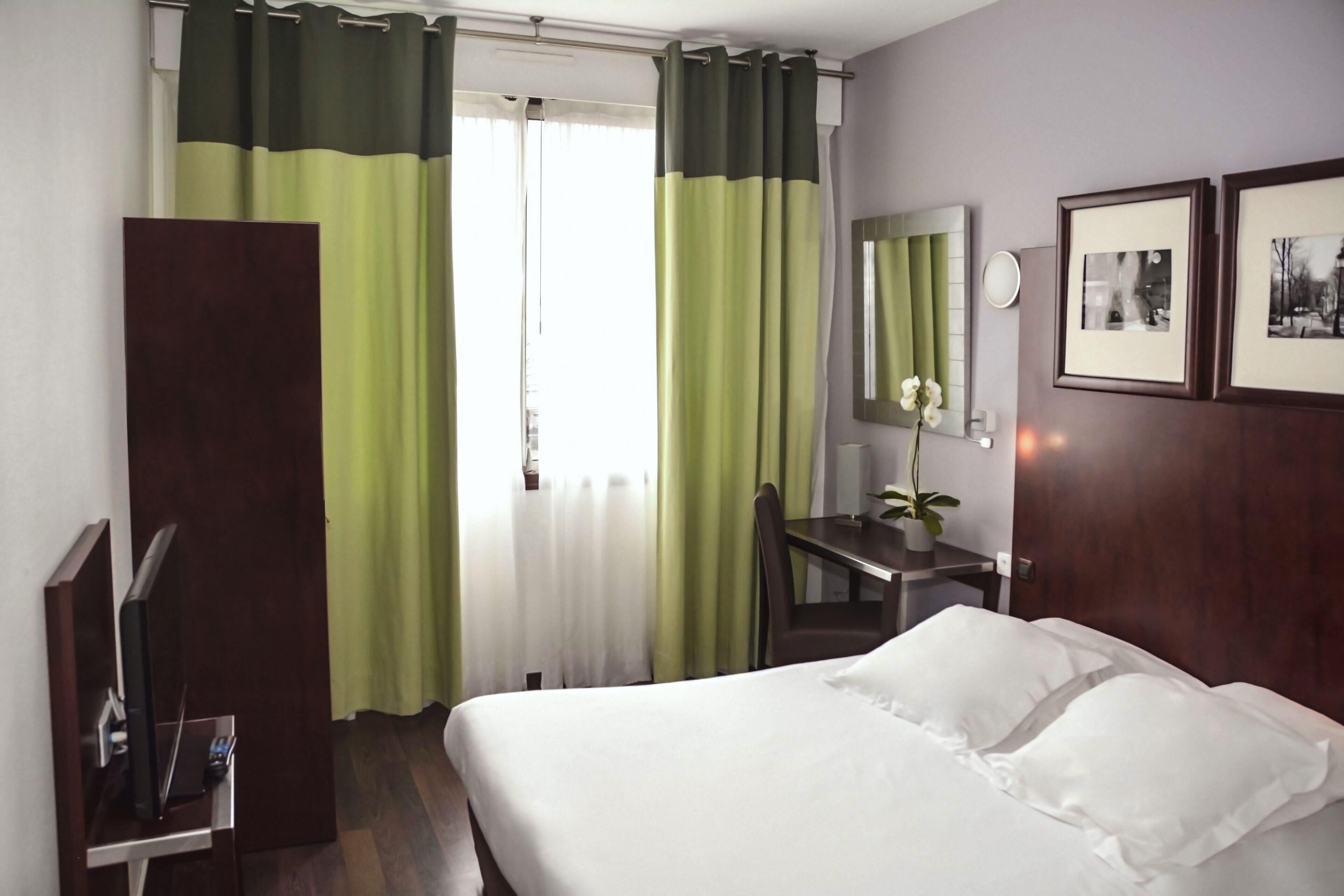 A hotel room with a bed, a desk, a chair, a TV, and curtains.