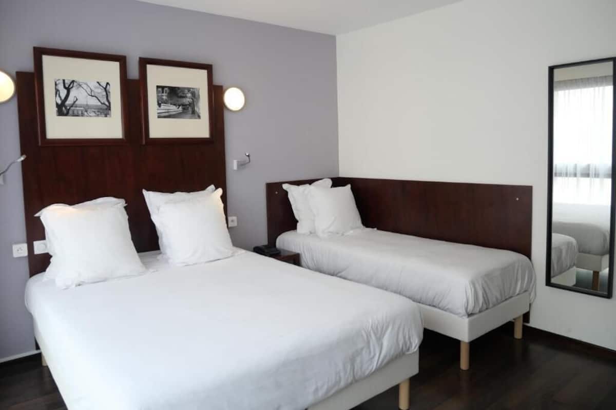 A hotel room with two single beds, a large mirror, and two framed pictures on the wall.