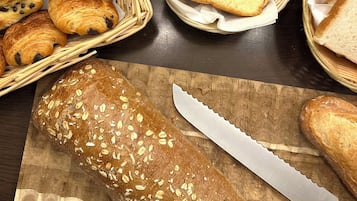 Diverse broden, waaronder croissants, sneetjes brood en een brood met havermout, op een houten tafel.