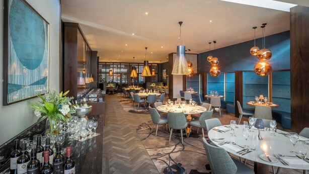 A modern restaurant with round tables, blue chairs, and hanging pendant lights.