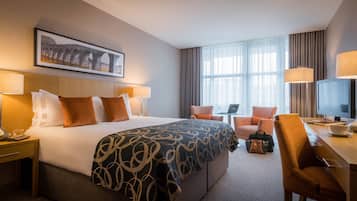 Hotelkamer met een groot bed, twee nachtkastjes met lampen, een bureau met stoel, een televisie en een raam met gordijnen.