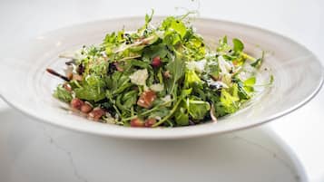 A white plate with a salad on a white marble surface.