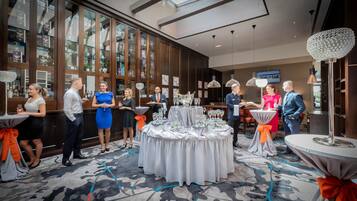 Un evento formal en una sala amplia con grandes ventanales, una mesa central con mantel blanco y una araña.