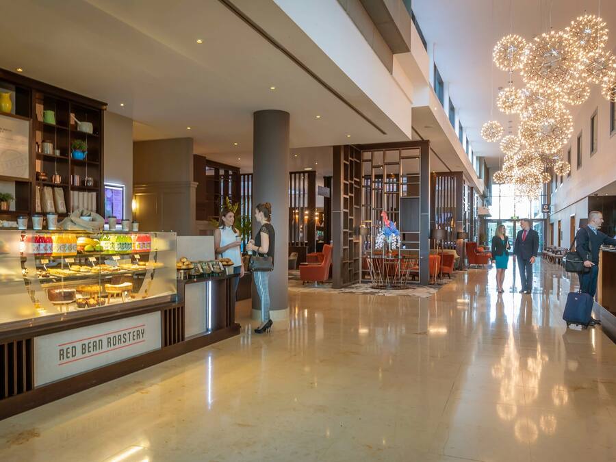 A modern hotel lobby with a coffee shop, a reception desk, and a spacious seating area.