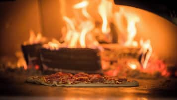 A pizza in a wood-fired oven with flames visible in the background.